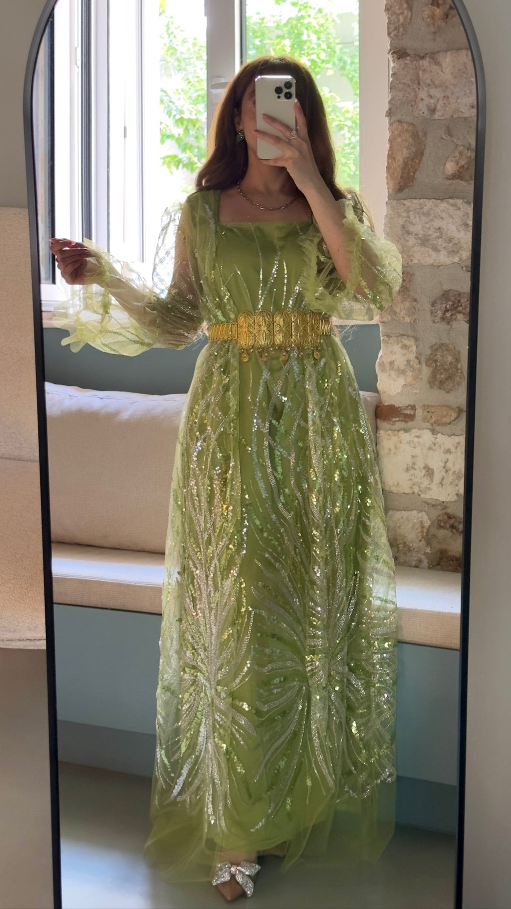 Woman wearing a green sequined dress with a yellow belt in front of a mirror.