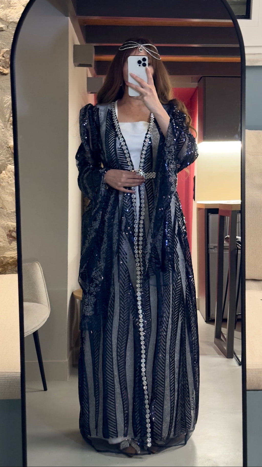Person wearing a long, dark blue sequined dress in a room with a mirror.