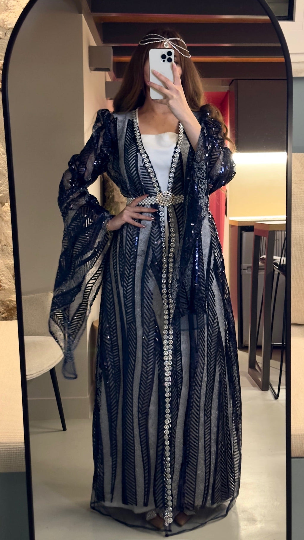 Person wearing a long, dark blue dress with white patterns in front of a mirror.