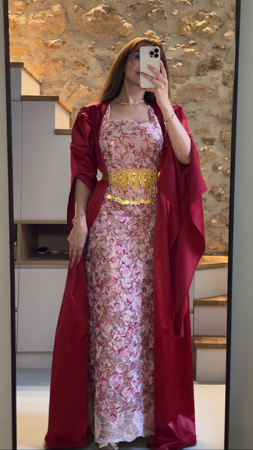 Person wearing a floral dress with a red cover-up in front of a stone wall.