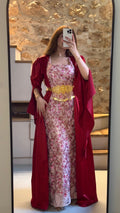 Person wearing a floral dress with a red cover-up in front of a stone wall.