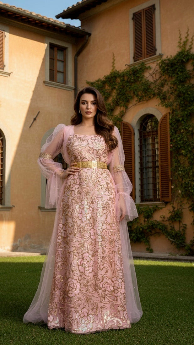 Woman in a pink lace dress standing in front of a villa with greenery.
