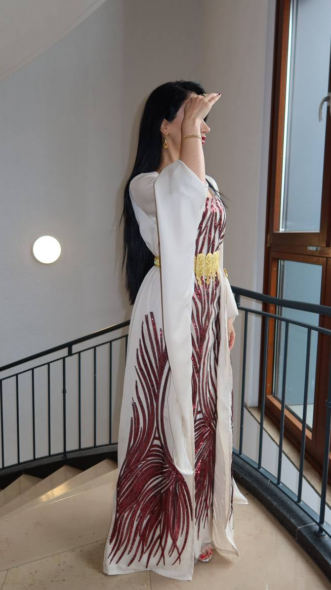 Woman in a long, patterned dress standing on a staircase with a window in the background.