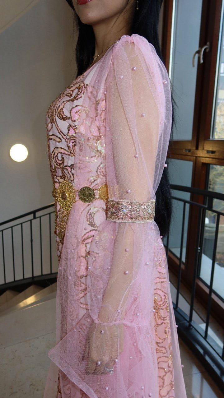 Person wearing a pink embroidered traditional outfit with gold details indoors.
